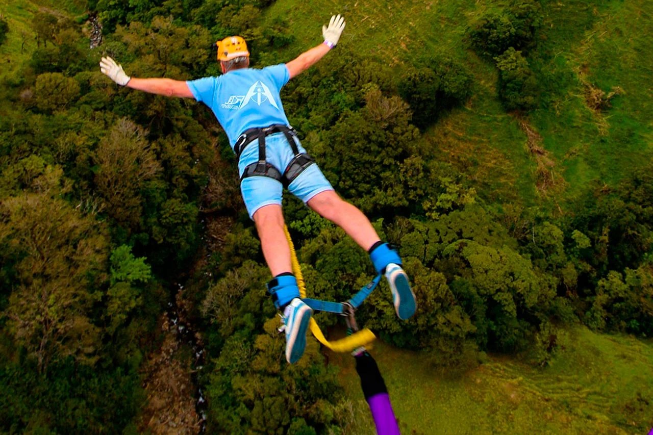 A person in a blue dress doing bungee jumping over a lush green forest of Manali