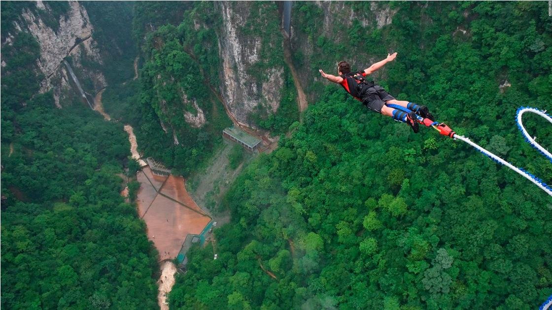Person bungee jumping over lush green canyon.