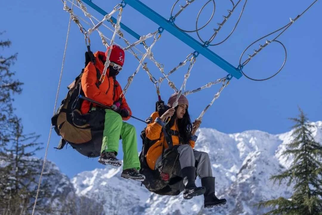Two people are doing a giant swing over snow-capped mountains on a clear day.