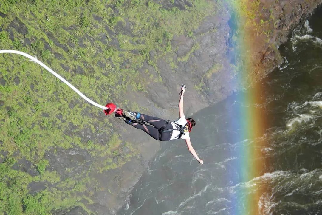 Woman bungee jumping over Victoria Falls with a rainbow in the background.