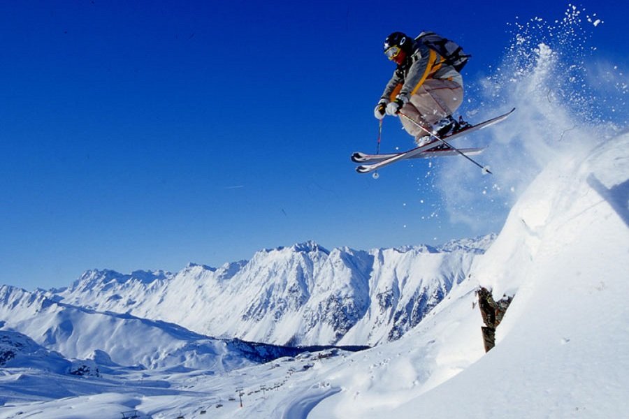Skier performing jump with snowy mountains and clear blue sky