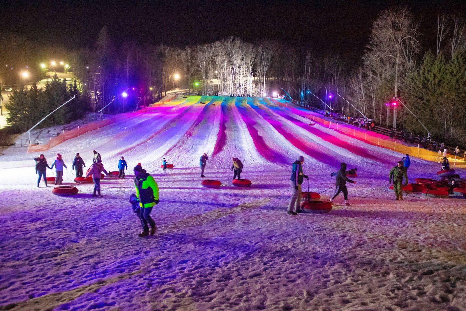 Nighttime snow tubing hill with colorful lights and people enjoying winter activities.