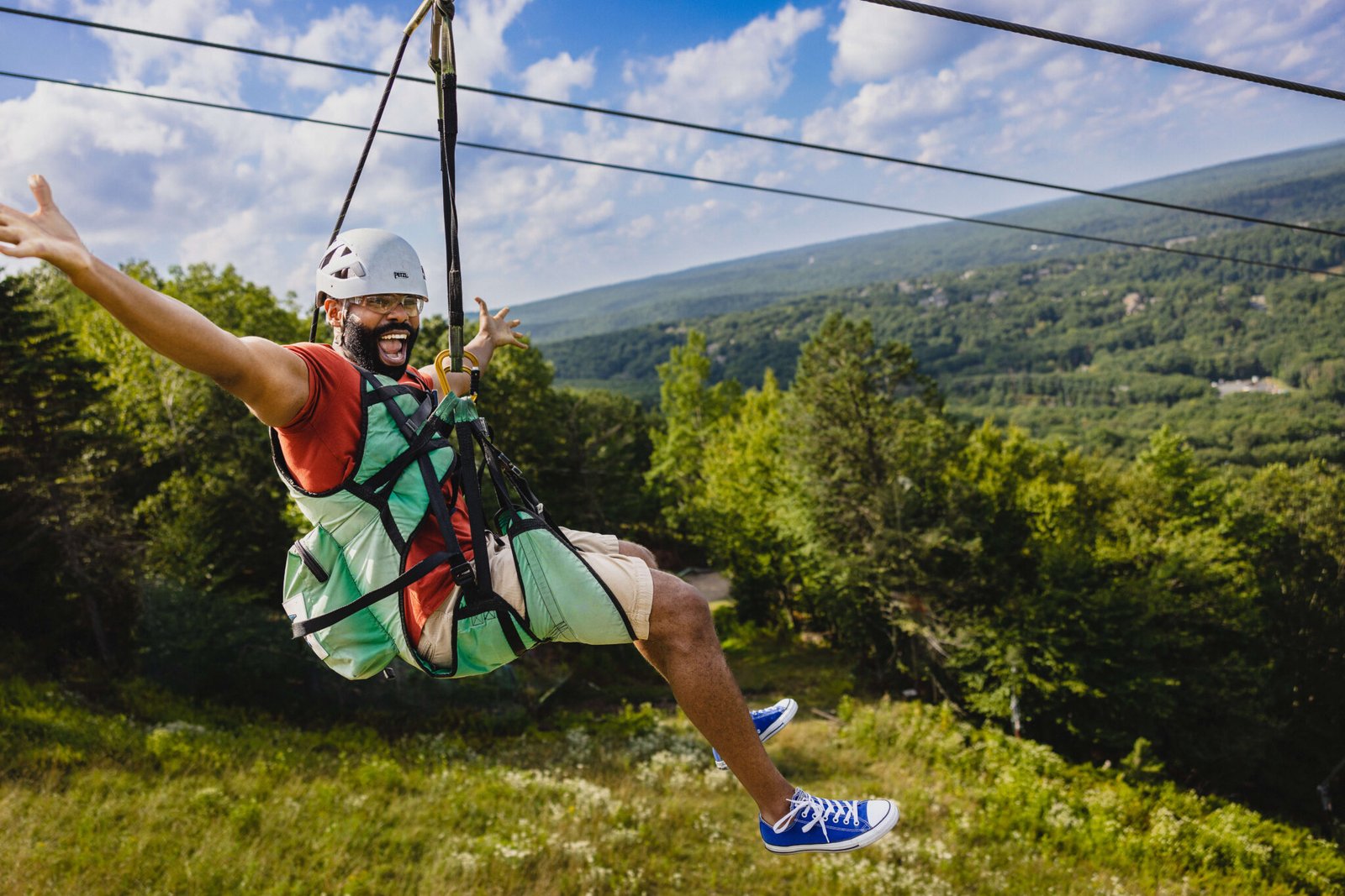 Excited man ziplining over the lush green landscape of Manali, with a clear blue sky and scenic mountain views in the background.